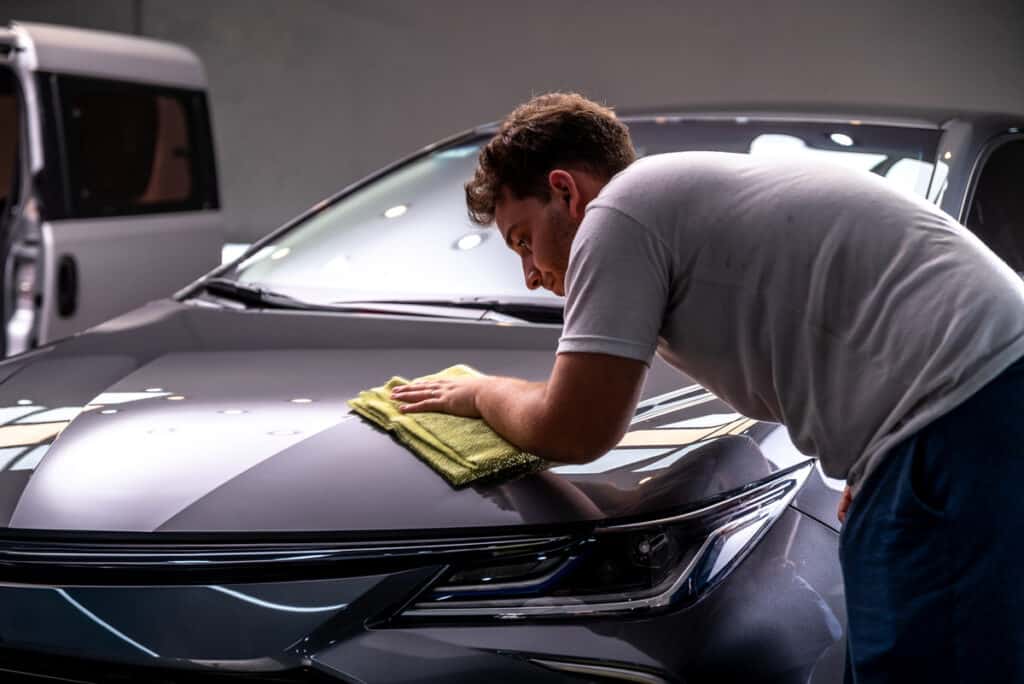 Détailing voiture: Polissage auto et protection carrosserie Homme polissant le capot d'une voiture sombre avec un chiffon microfibre jaune. Détailing automobile professionnel.