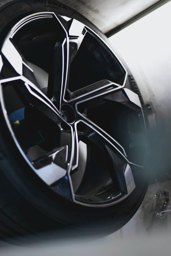 Jante sport Potenza : design automobile haute performance Jante de voiture noire et argentée au design complexe, pneu "POTENZA SPORT" visible. Surfaces brillantes en atelier automobile.