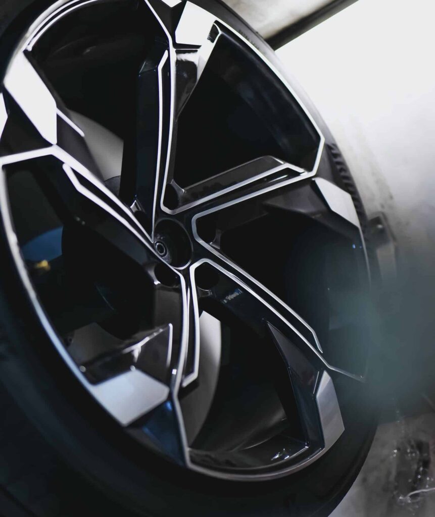 Jante sport Potenza : design automobile haute performance Jante de voiture noire et argentée au design complexe, pneu "POTENZA SPORT" visible. Surfaces brillantes en atelier automobile.