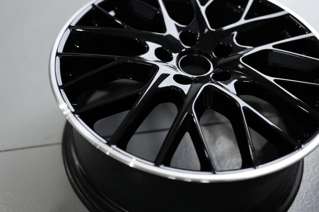 Jante voiture sport noire polie – Design élégant Jante de voiture noire brillante à rayons multiples et bord argenté poli sur fond clair.