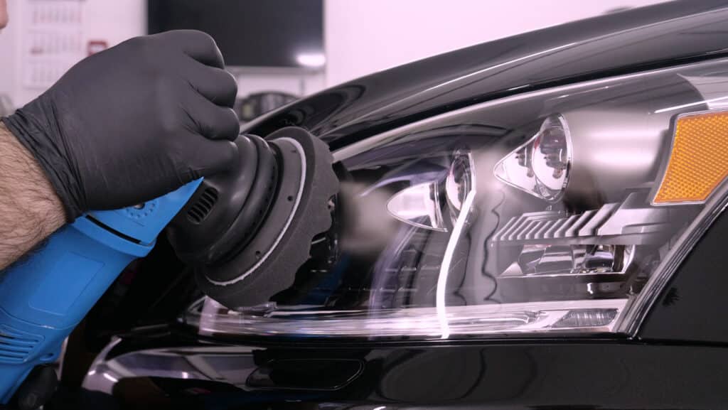 Polissage Professionnel de Phares de Voiture Noire Main d'un professionnel gantée polissant le phare et le capot noirs d'une voiture avec une lustreuse bleue. Surface brillante reflétant l'atelier.