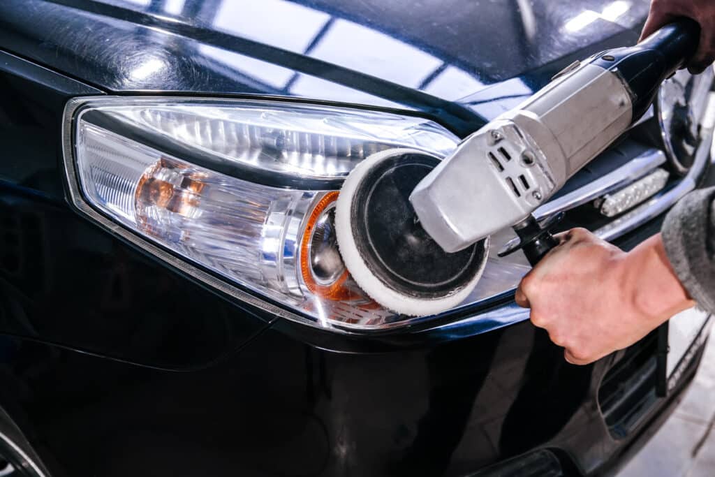 Polissage phare voiture: Rénovation et brillance auto Mains polissant un phare de voiture noire avec une machine. La carrosserie présente des reflets et des micro-rayures.